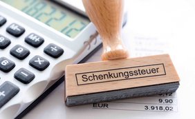 Schenkungsteuer: Einlage eines Familienheims in eine Ehegatten-GbR Taschenrechner und daneben ein Stempel mit Schenkungsteuer bedruckt